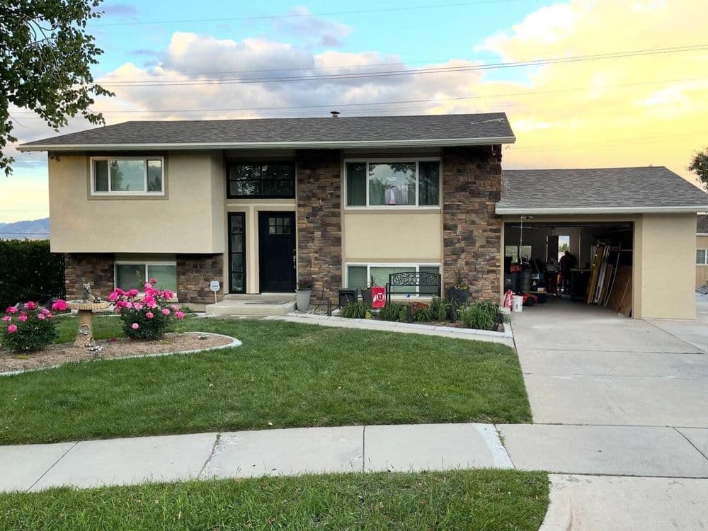 Split-level home with stone accents, driveway, and landscaped yard featuring pink flowers.