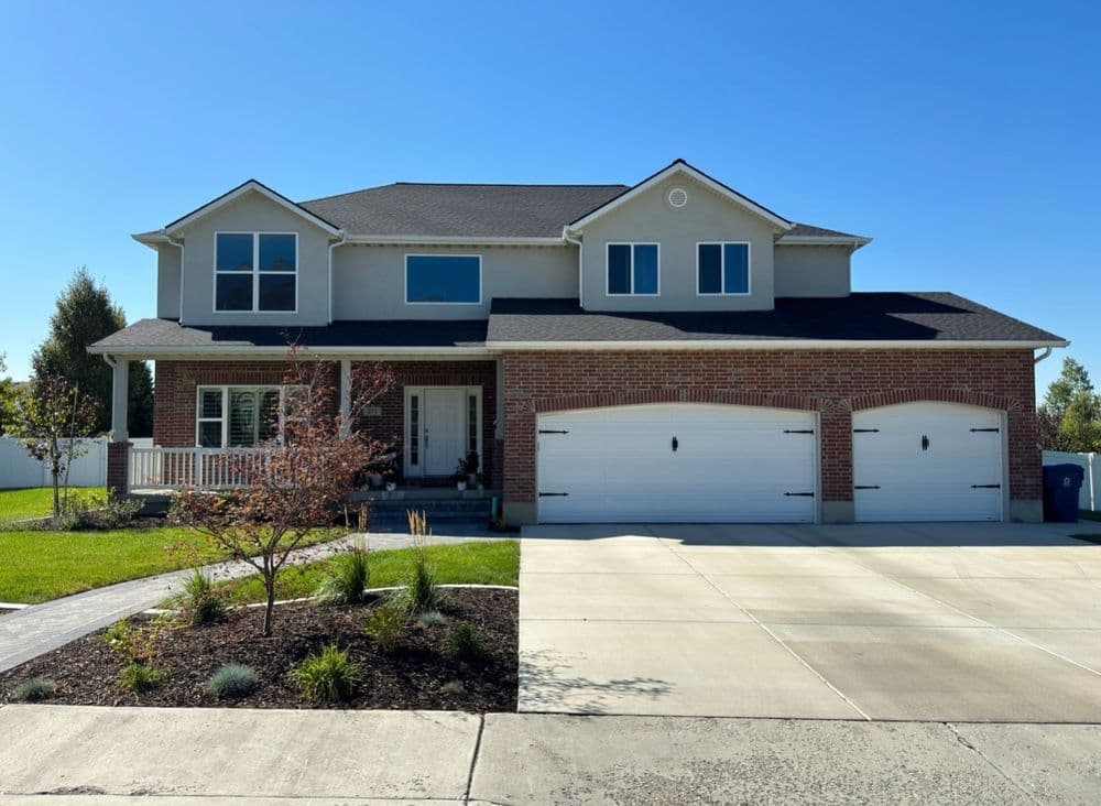 Modern two-story brick house with a front porch, two-car garage, and landscaped yard.