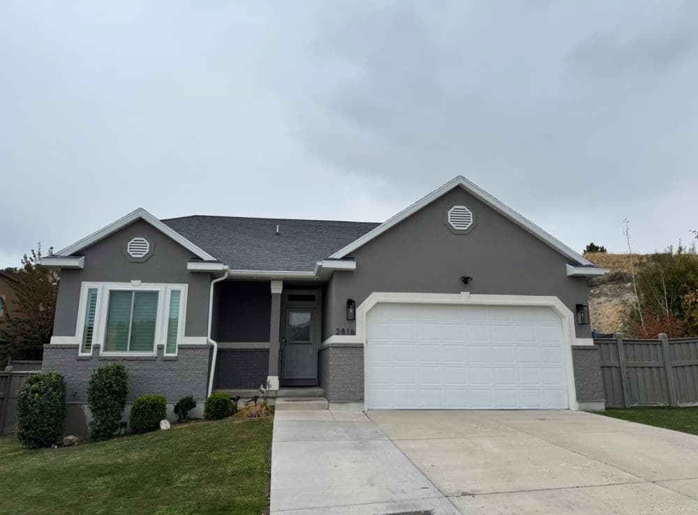 Gray modern house with a garage, green lawn, and cloudy sky in the background.