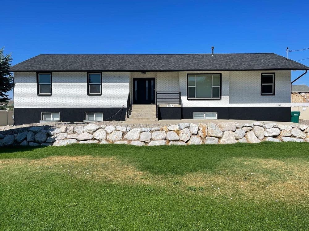 Two-story modern home with black roof, white brick exterior, and stone landscaping.