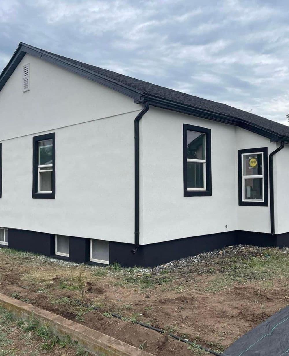 Modern white house with black accents and new windows, set on a grassy lot.