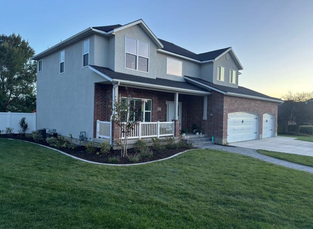 Two-story modern house with brick facade, garage, and landscaped yard at sunset.