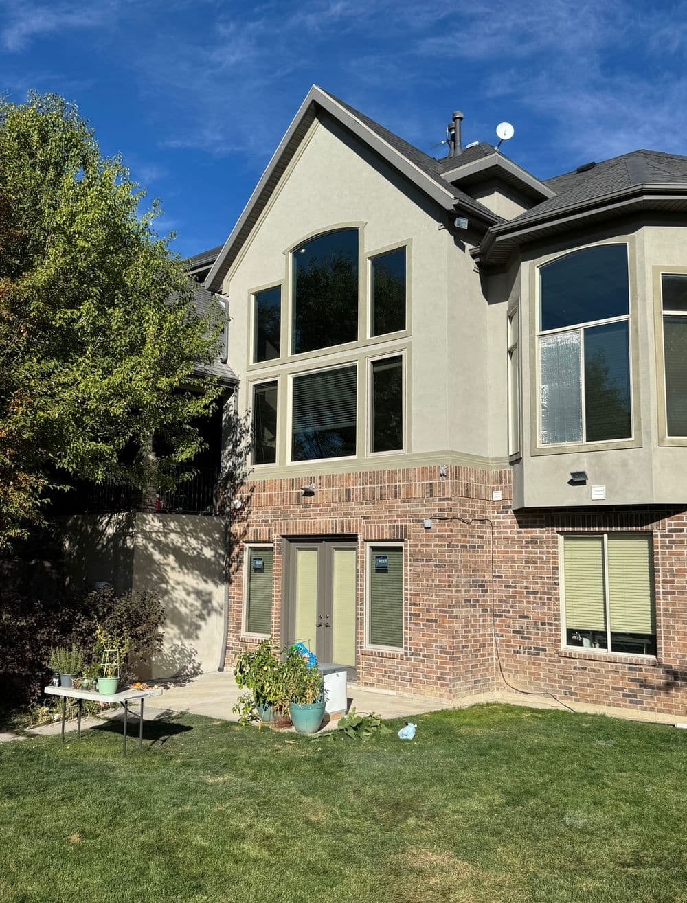 Modern two-story home with large windows, brick exterior, and lush backyard garden.