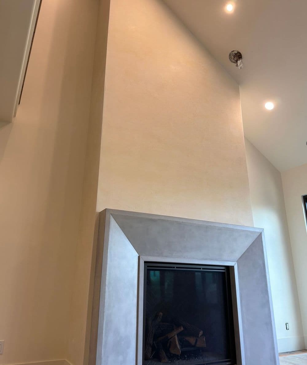 Modern fireplace with a sleek concrete surround and textured wall in a well-lit room.