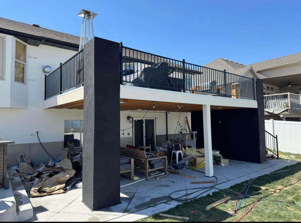 Modern outdoor deck with black railing, patio furniture, and construction materials below.