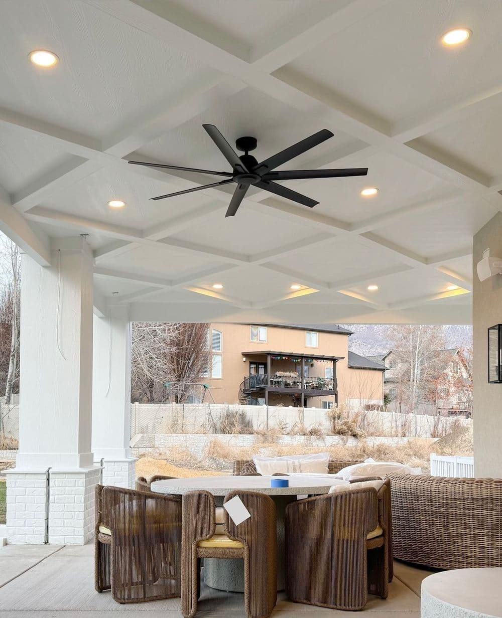 Elegant outdoor patio with ceiling fan, stylish furniture, and scenic hillside view.