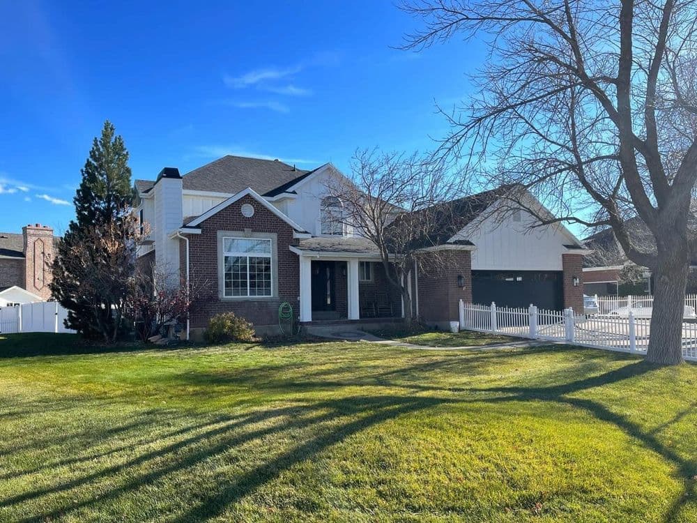 Two-story brick house with white accents and a spacious front yard under a clear blue sky.