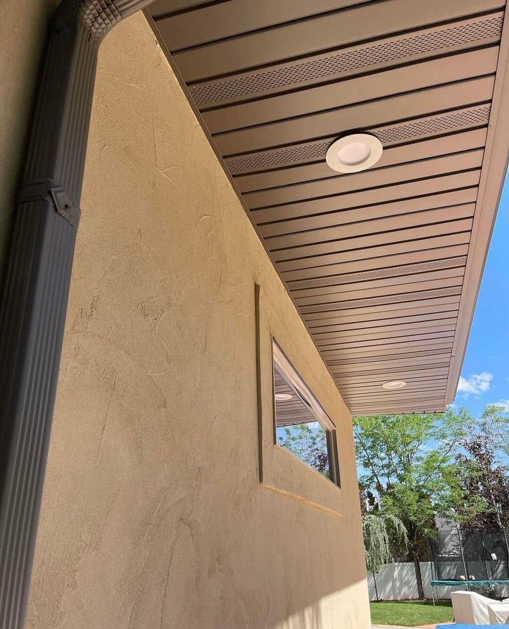 Modern home exterior with metal roof and recessed lighting against a clear blue sky.