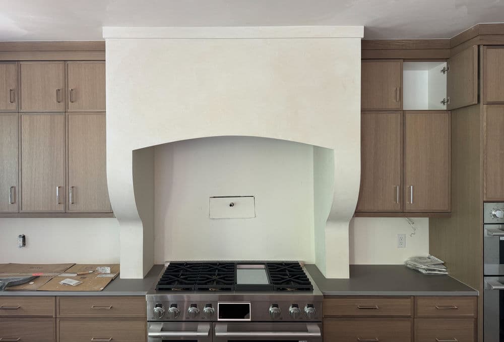Modern kitchen design featuring dark countertops, wooden cabinets, and a stylish hood vent.