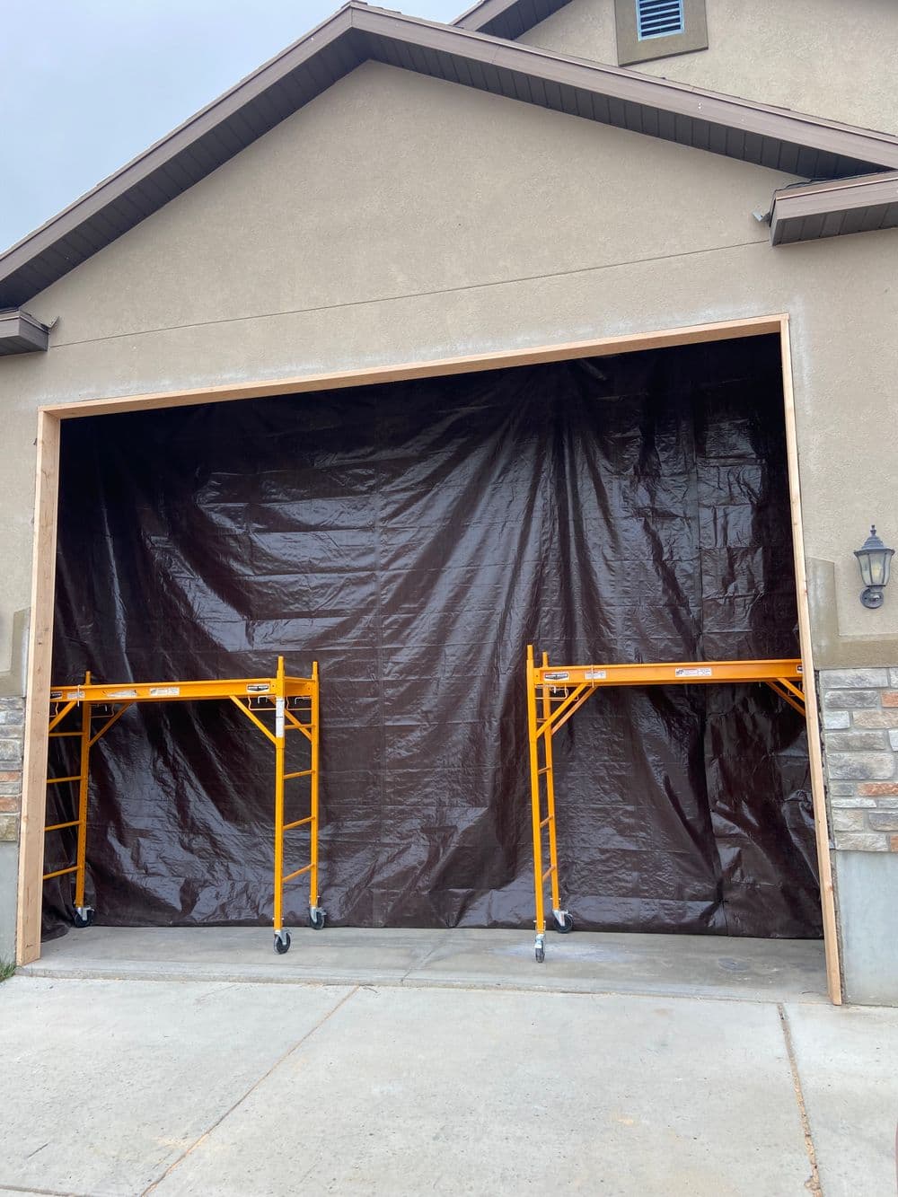 Scaffolding set up in front of a brown tarp covering a garage opening.