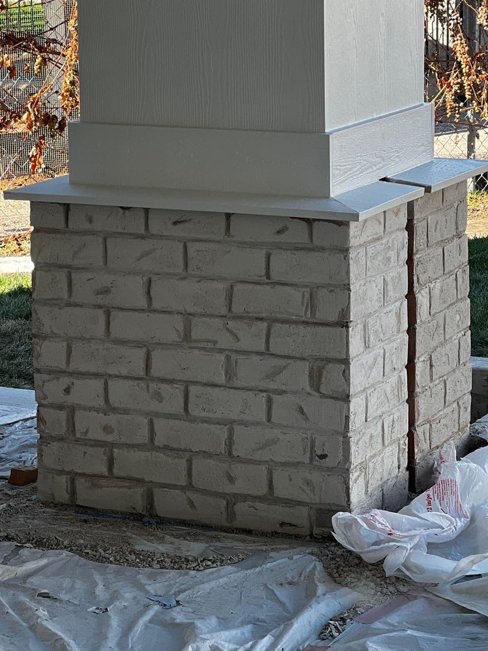 Brick pillar construction with white trim, surrounded by construction debris and tools.