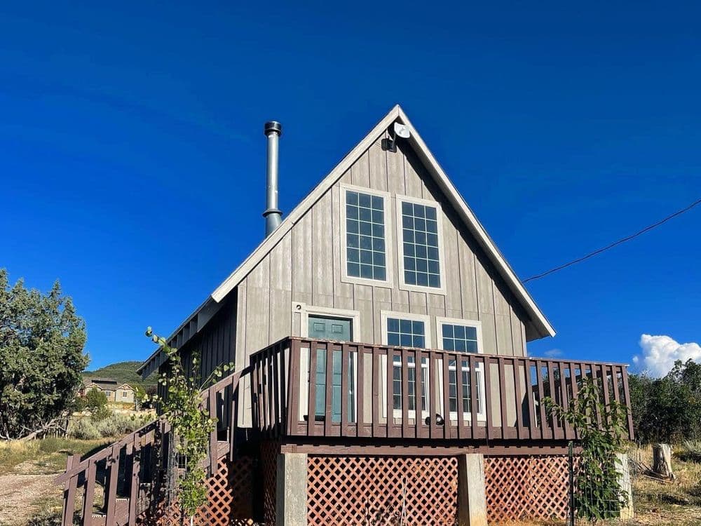 Charming A-frame house with a deck, blue sky, and modern design in a scenic location.
