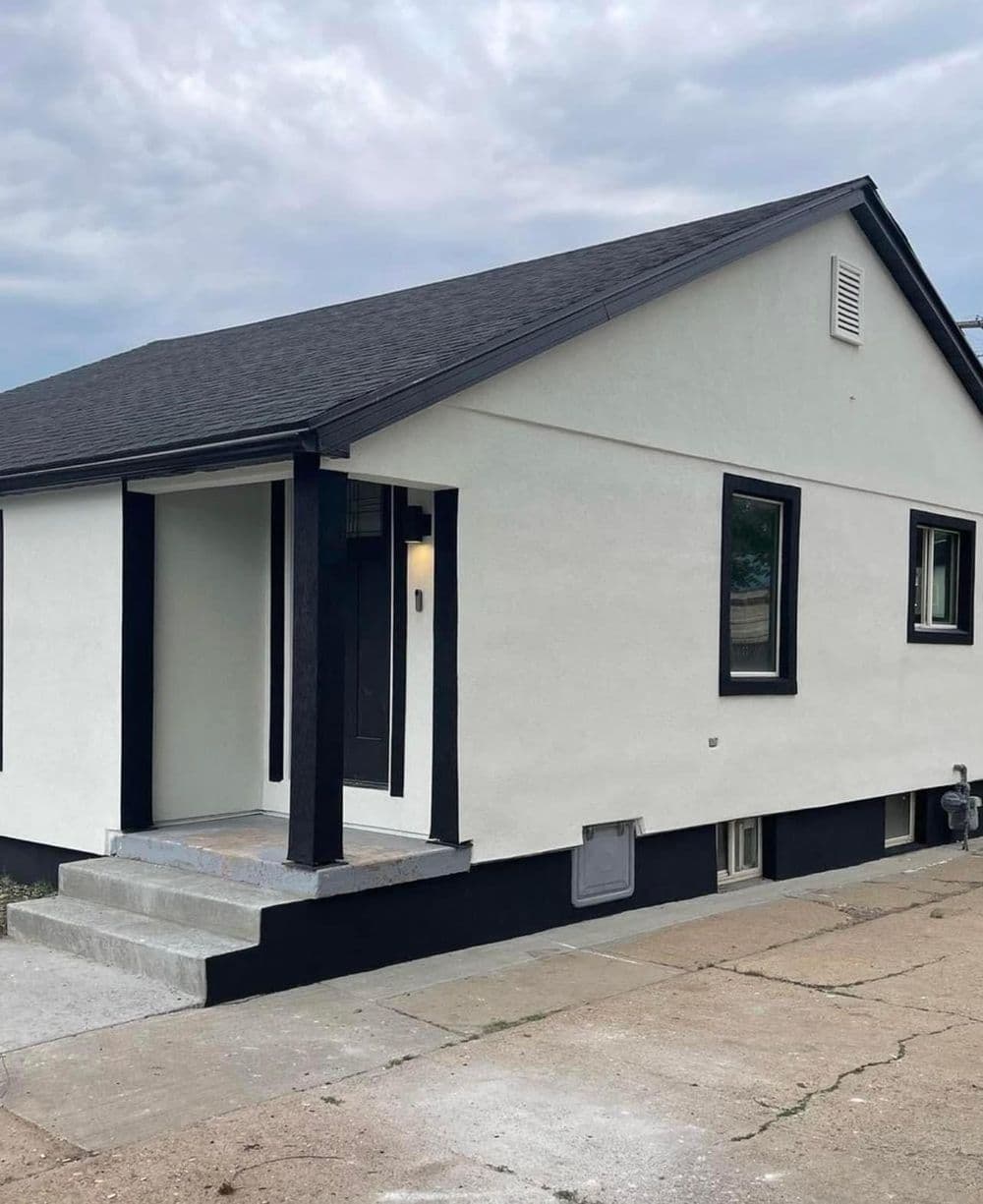 Modern single-story home with black trim and a welcoming porch, surrounded by paved pathway.