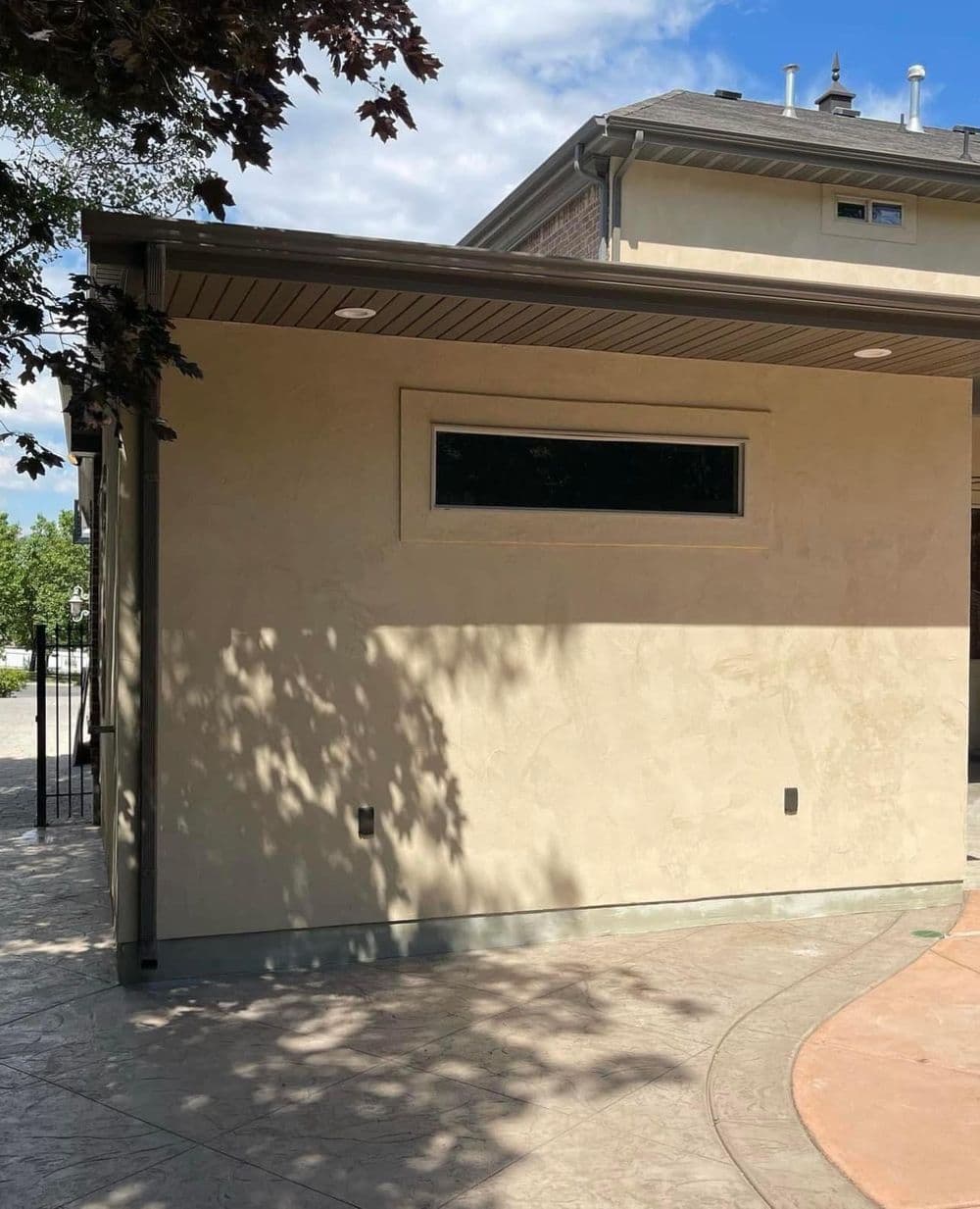 Modern exterior of a light-colored stucco house with a sleek window and shaded area.