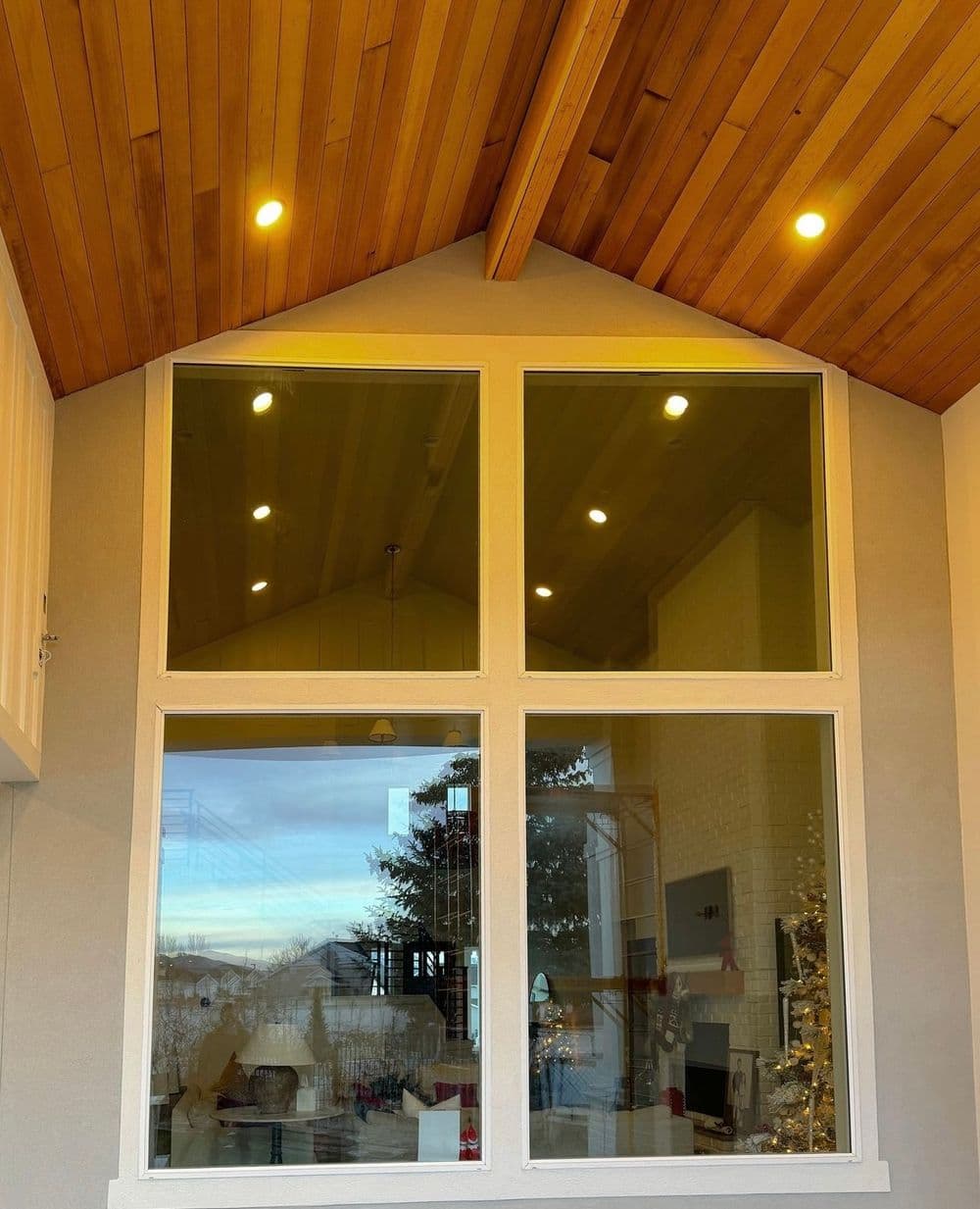 Modern home interior featuring large windows, wooden ceiling beams, and warm lighting.