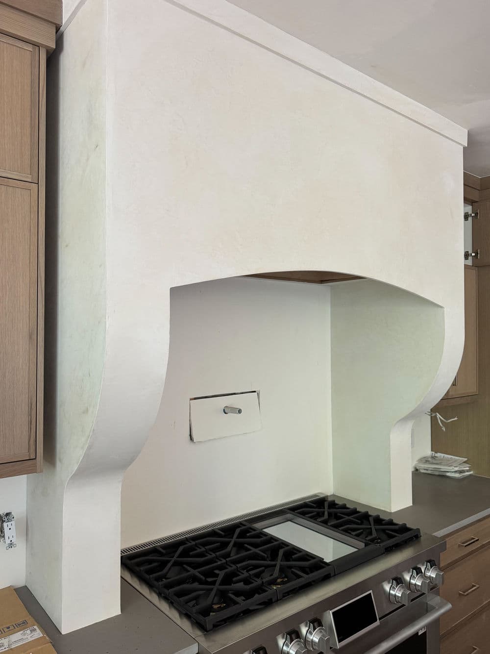 Modern kitchen hood with elegant curve above gas cooktop, featuring sleek cabinetry and countertops.