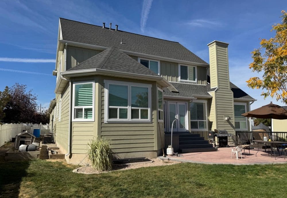 Modern two-story home with light green siding, patio, and outdoor seating area.