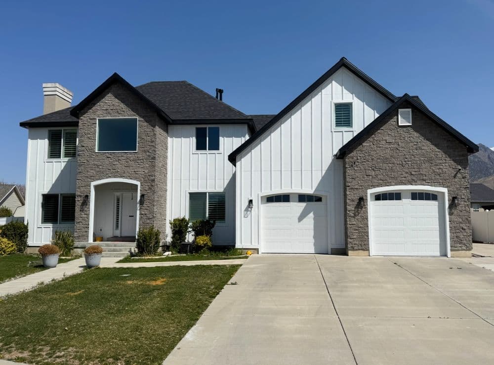 Modern two-story house with stone and white siding, featuring a two-car garage and landscaped yard.