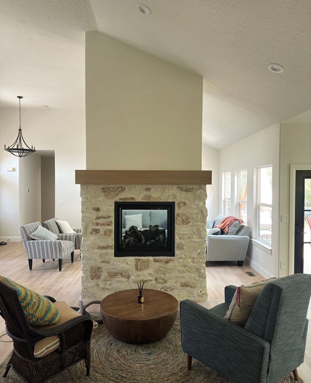 Modern living room featuring a central stone fireplace, cozy seating, and natural light.