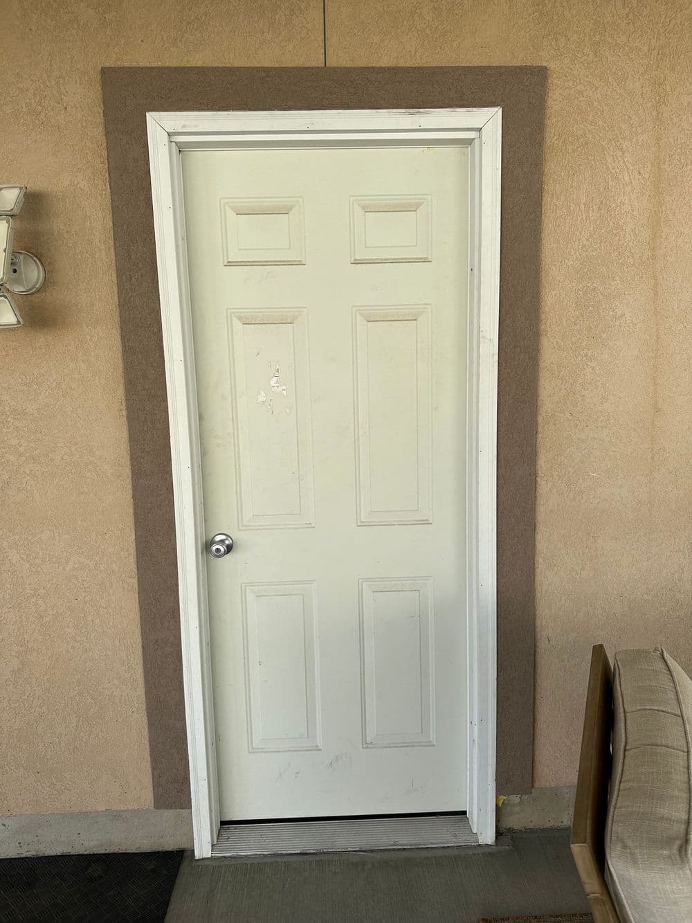 White door with four panels and a light brown trim on a beige wall.