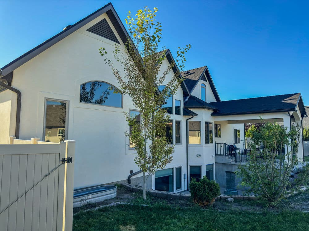 Modern residential home with large windows, a tree, and outdoor patio space in a sunny setting.