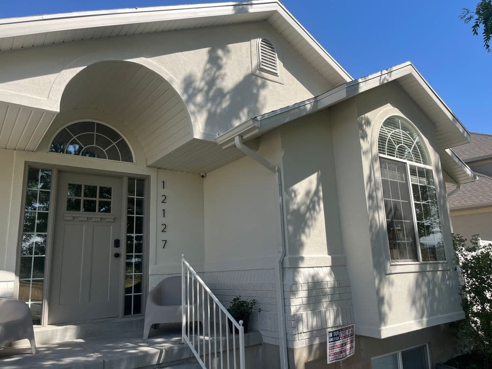 White modern home exterior with a front porch, large windows, and landscaped entrance.