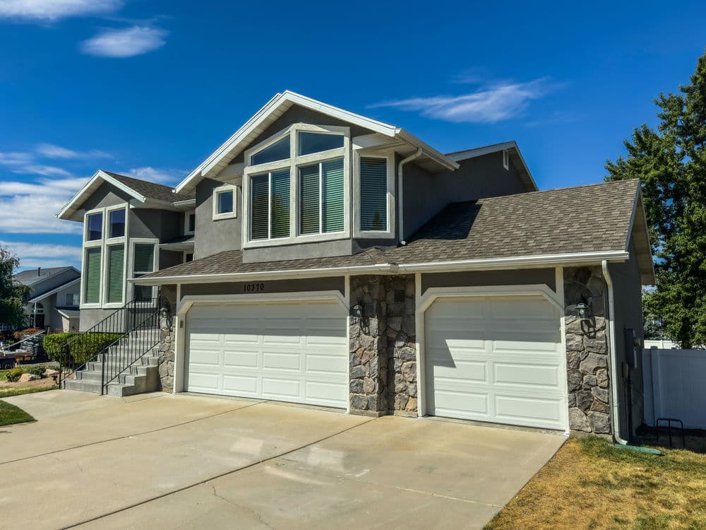 Modern gray house with large windows and dual garage doors on a sunny day.