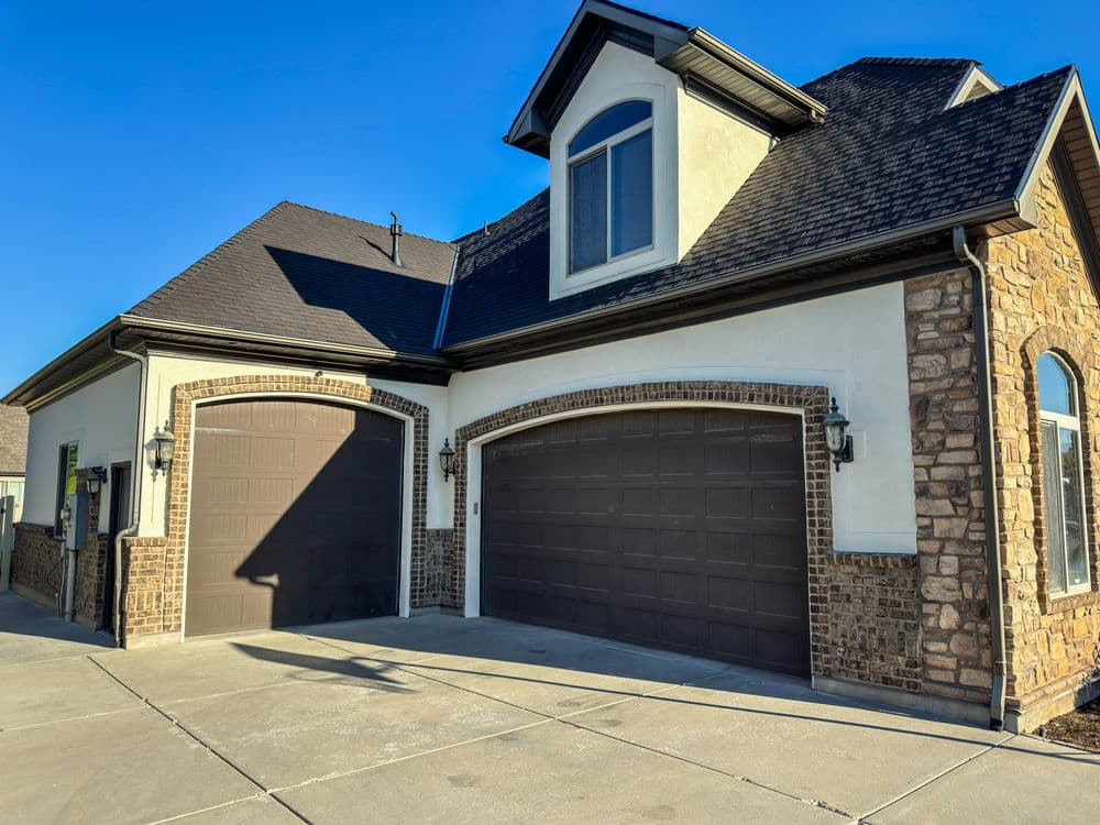 Modern two-car garage with stone accents and large windows under a clear blue sky.