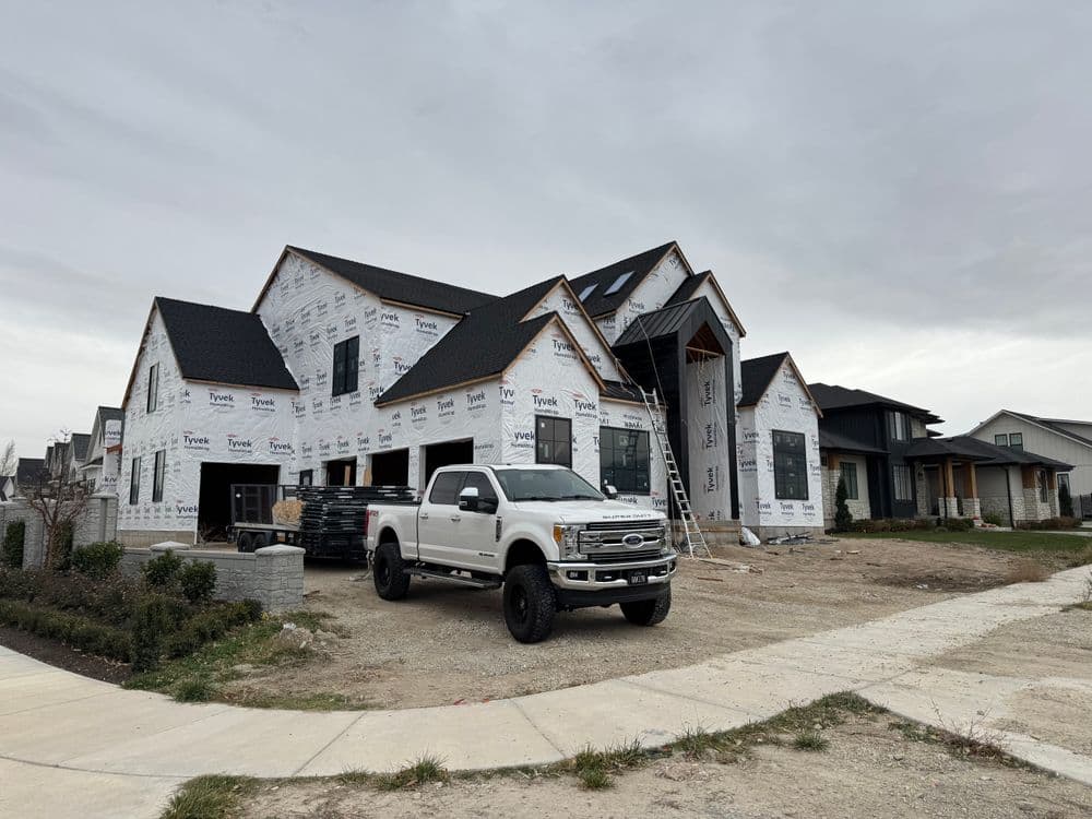 Construction site of a new home with truck parked in front and scaffolding visible.