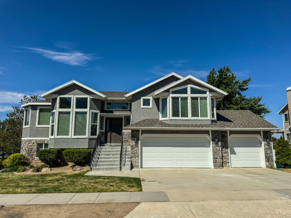Modern two-story gray house with stone accents and large windows, featuring a three-car garage.