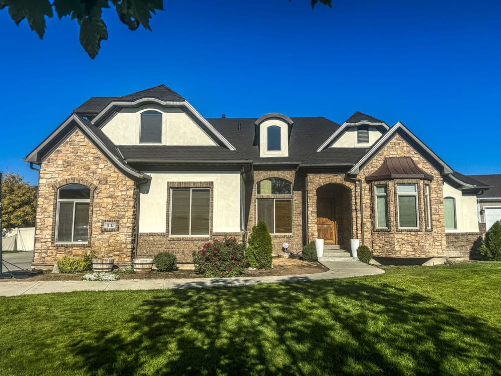 Beautiful stone-front house with a landscaped yard and clear blue sky. Ideal family home exterior.