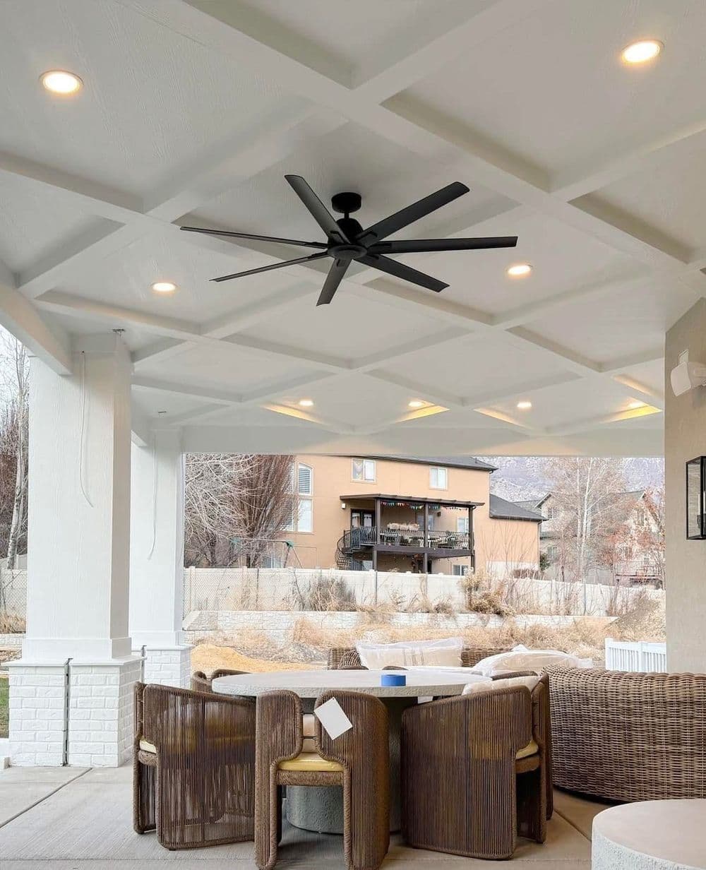 Outdoor patio with modern ceiling fan, wicker furniture, and scenic residential backdrop.