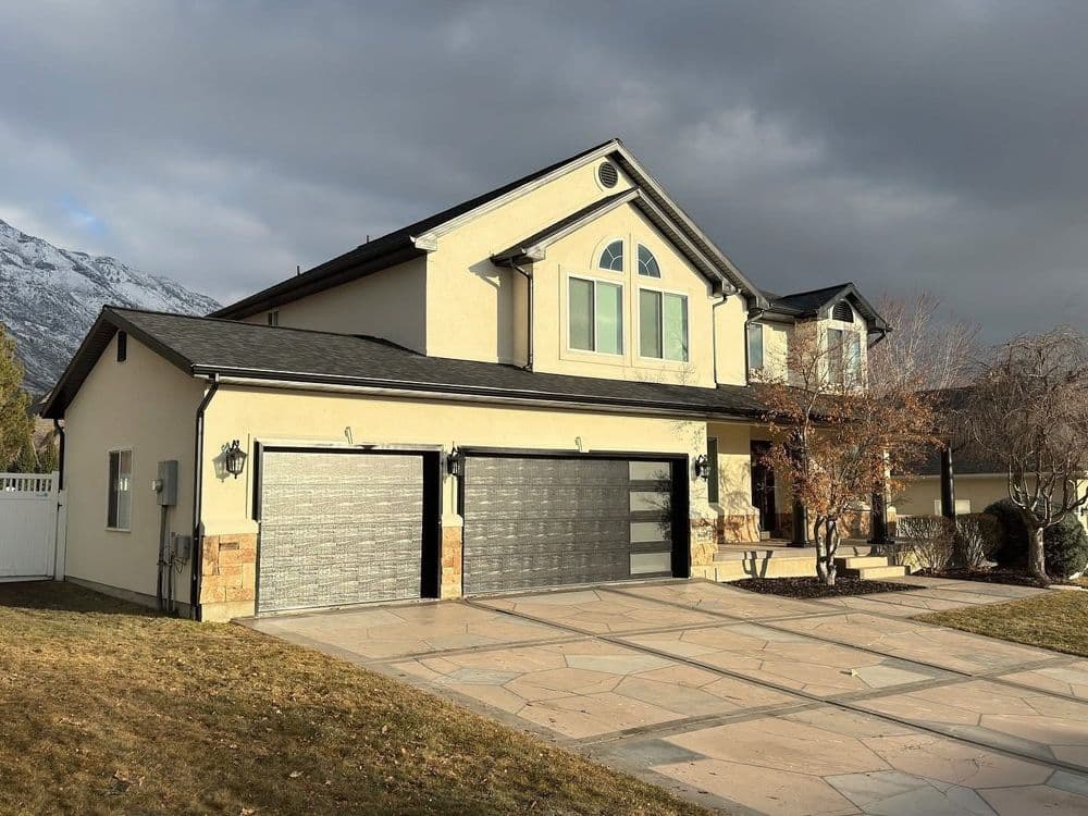 Modern two-story house with double garage and landscaped driveway under cloudy sky.