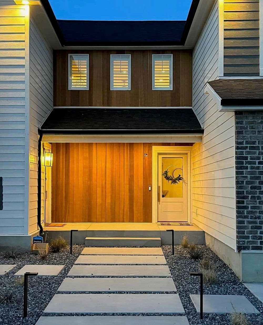 Modern home exterior with warm lighting, wooden accents, and a welcoming entryway.